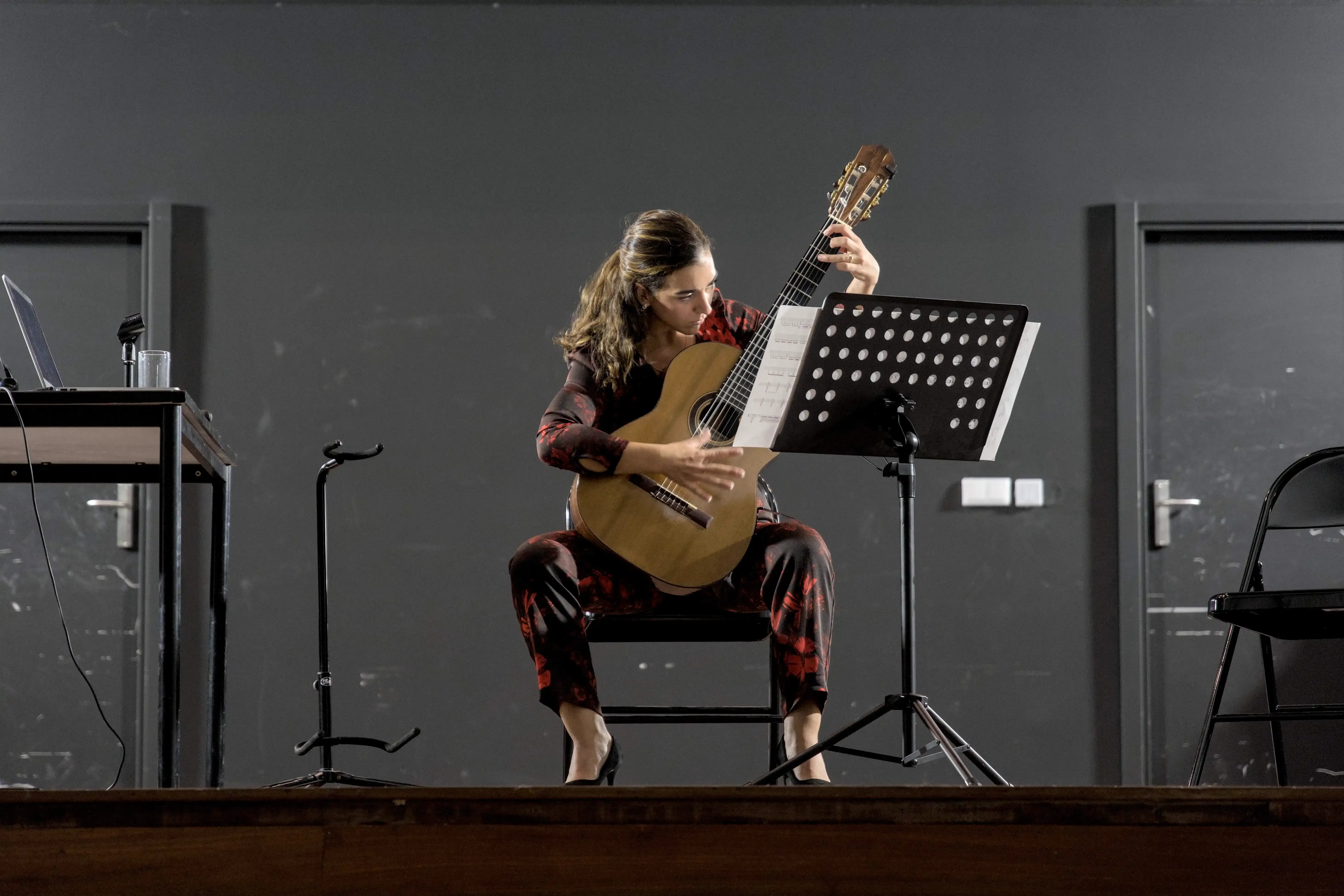Uma mulher toca guitarra clássica num palco.